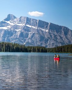 two people in a red canoe on a lake with mountains in the background