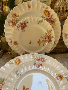 there are many plates on the table with flowers painted on them and one has a clock in the background