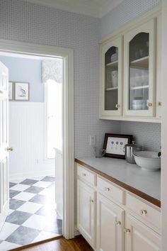 a kitchen with white cabinets and checkered flooring on the walls is seen through an open door