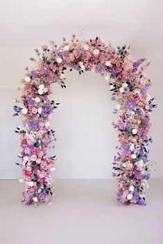 an arch made out of flowers is shown in the middle of a white room with pink and purple colors