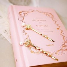 a pink notebook with two gold - tone hair pins on it