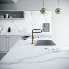 a white kitchen with marble counter tops and gold pendant lights hanging from the ceiling over the sink