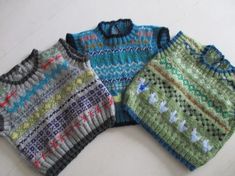 three knitted sweaters sitting next to each other on a white surface with one blue and the other green