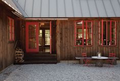 there is a table and chairs in front of the house with red doors on it