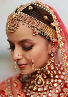 a woman wearing a red and gold bridal outfit with pearls on her head, nose ring