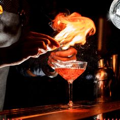 the bartender is pouring his drink into the glass with flames coming out of its mouth