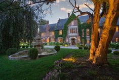 a large house with lots of trees and bushes in front of it at night time