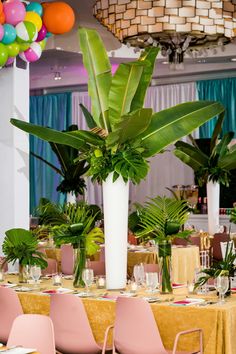 the tables are set with pink chairs and green plants in tall vases on them