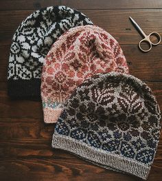 three knitted hats sitting on top of a wooden floor next to scissors and yarn