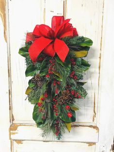 a christmas wreath hanging on the side of a door with red bows and pine cones