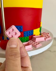 a hand is pointing at a lego cake with pink and yellow blocks on it,