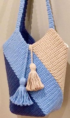 a crocheted bag hanging on the wall with a tasseled handle and two different colors