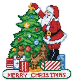 a cross stitch christmas tree with santa claus and presents on it, next to a small dog