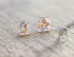 two small square shaped earrings on top of a wooden table with white and orange designs