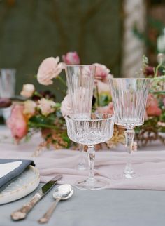 there are three glasses on the table with silverware next to it and flowers in the background