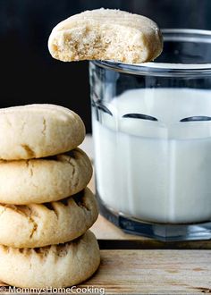 a stack of cookies next to a glass of milk on a wooden table with a cookie in the foreground