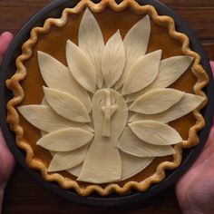 a person holding a pie with white flowers on the top and leaves in the middle