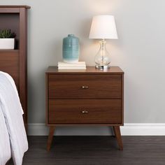 a nightstand with a lamp on it next to a bed