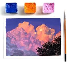 three different colored clouds are in the sky above some watercolor paints and pencils