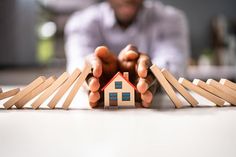 a person holding a small house in front of some books on the table with their hands