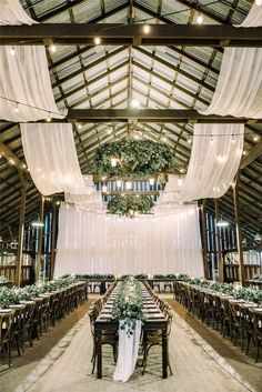 an indoor venue with tables and chairs covered in white draping, greenery and hanging lights