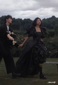 a man and woman dressed in black holding hands while standing next to each other on a bench