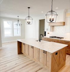 an empty kitchen with wooden cabinets and white marble counter tops, two pendant lights hanging over the island