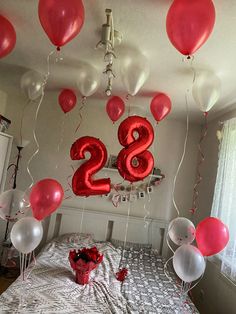 red and white balloons are floating in the air above a bed with a number twenty sign on it