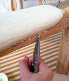 a person holding a pair of scissors in front of a wooden chair with fabric on it