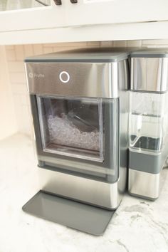 a stainless steel appliance sitting on top of a marble countertop next to a blender with ice in it