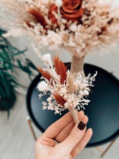 a person holding a dried flower in front of a vase with flowers on top of it