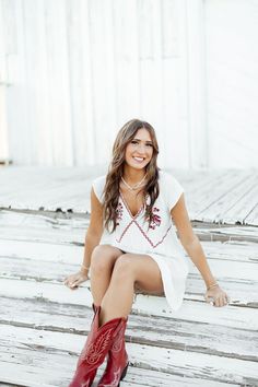 a woman sitting on top of a wooden floor wearing red cowboy boots and a white dress