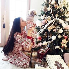 a woman sitting in front of a christmas tree with presents on the floor next to her