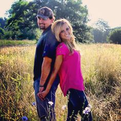 a man standing next to a woman in a field with tall grass and wildflowers