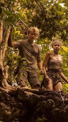 two men and a woman are walking through the jungle on a log in front of some trees