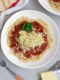 two plates of spaghetti with broccoli, cheese and bread next to it on a table