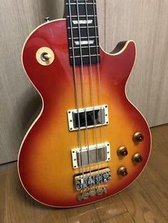 a red and yellow bass guitar sitting on top of a hard wood floor next to a wall