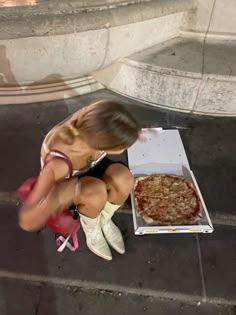 a woman kneeling down next to a pizza box