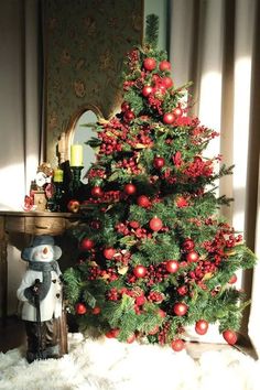 a small christmas tree with red ornaments on it and a snowman next to it