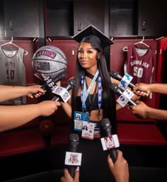 a woman in a graduation cap and gown surrounded by microphones with basketballs on them