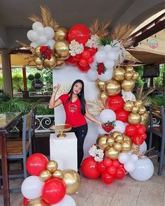 a woman standing in front of a bunch of red, white and gold balloon decorations