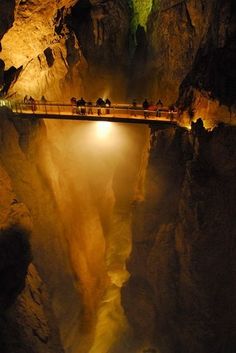 people standing on a bridge over a river in a canyon at night with the lights on