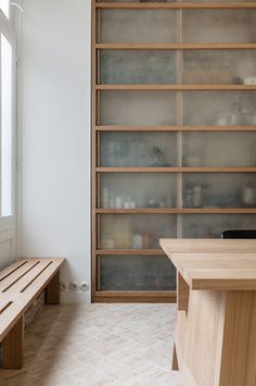 a wooden bench sitting in front of a book shelf next to a window on top of a tiled floor