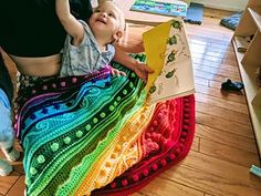 a woman sitting on the floor holding a baby in her lap and looking up at an open book