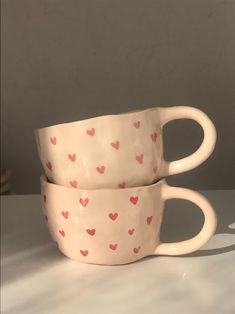 two coffee cups with hearts on them sitting side by side in front of a wall