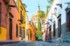 a car is parked on the cobblestone street in front of colorful buildings and palm trees