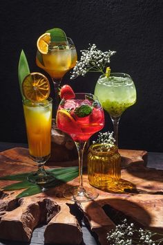 three different types of cocktails sitting on a wooden table next to rocks and flowers