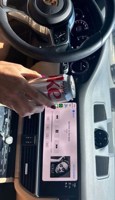 a person holding a cell phone in their hand near a car steering wheel and dashboard