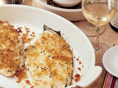 some food is on a white plate with wine glasses and other dishes in the background