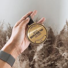 a hand holding a round gold award in front of some dry grass and plants with the words best hair brand written on it